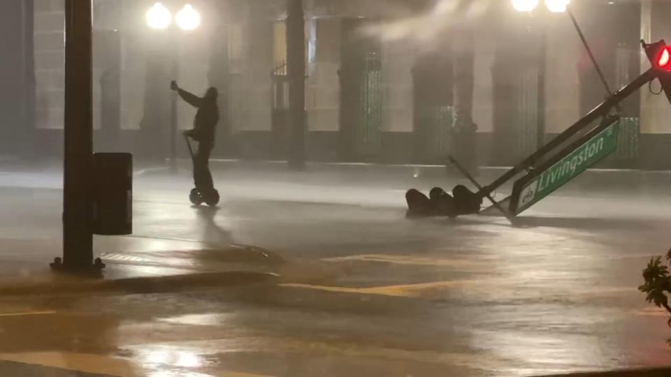 A person on a motorized scooter pauses near a fallen traffic sign as Ian's winds and rain move through downtown Orlando.