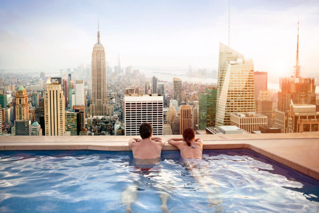 Two people relax in a rooftop pool overlooking NYC.