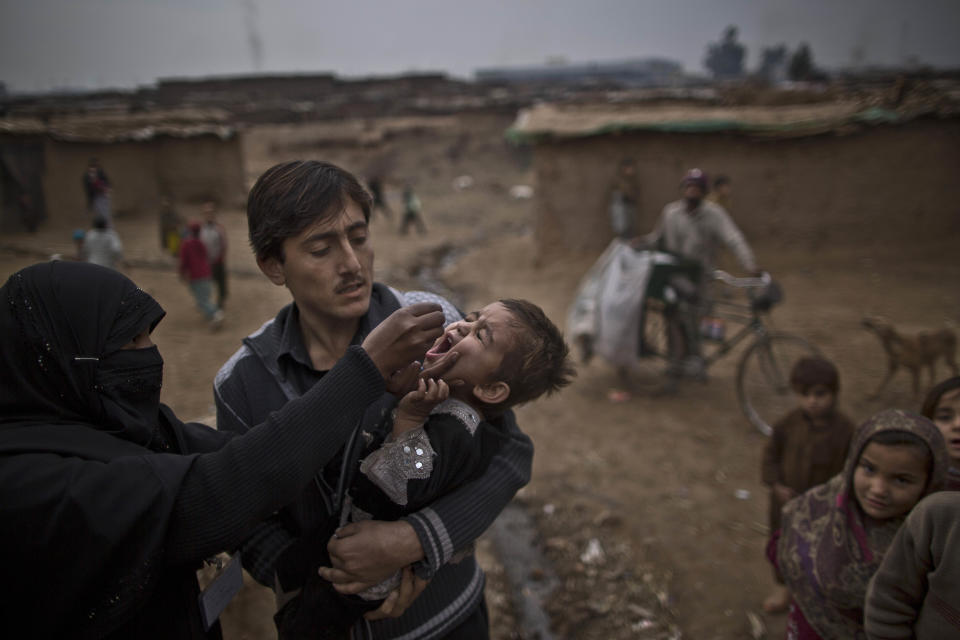 A Pakistani health worker, left gives a polio vaccine to a child, who was displaced with his family from Pakistan's tribal areas due to fighting between the Taliban and the army, in a poor neighborhood that hosts people displaced from tribal areas and Afghan refugees, on the outskirts of Islamabad, Pakistan, Wednesday, Jan. 22, 2014. Militants oppose vaccination against polio and consider such campaigns a cover for spying and also claim the vaccine is intended to make Muslim boys sterile. (AP Photo/Muhammed Muheisen)