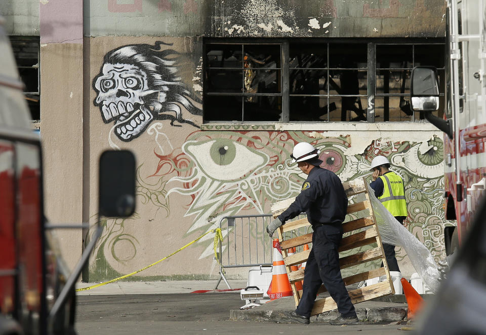 FILE - In this Wednesday, Dec. 7, 2016, file photo, a member of the Alameda County Sheriff's Department, left, carries away a pallet outside the site of a warehouse fire in Oakland, Calif. Two men who pleaded no contest to 36 charges of involuntary manslaughter will face the family members of those who died in the fire at an illegally converted Northern California warehouse. A two-day sentencing hearing for Derick Almena and Max Harris is scheduled to begin Thursday, Aug. 9, 2018, in Oakland. (AP Photo/Eric Risberg, File)