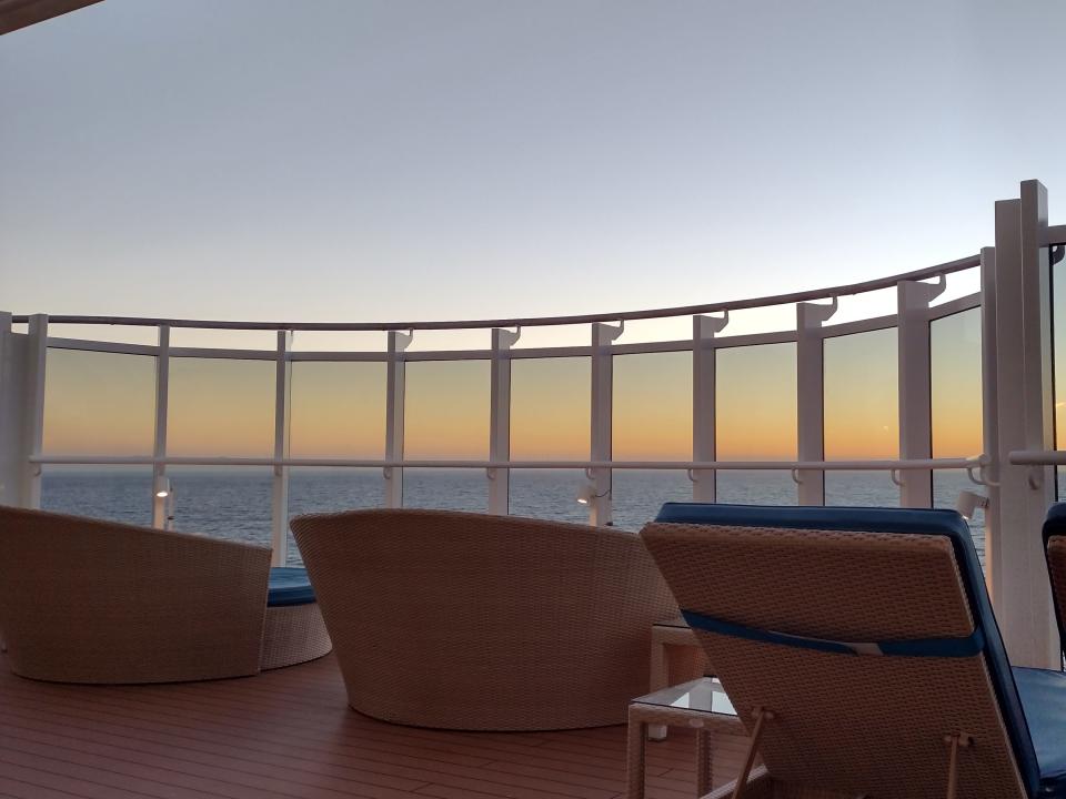 A sunset view as seen through a cruise ship deck with lounge chairs.