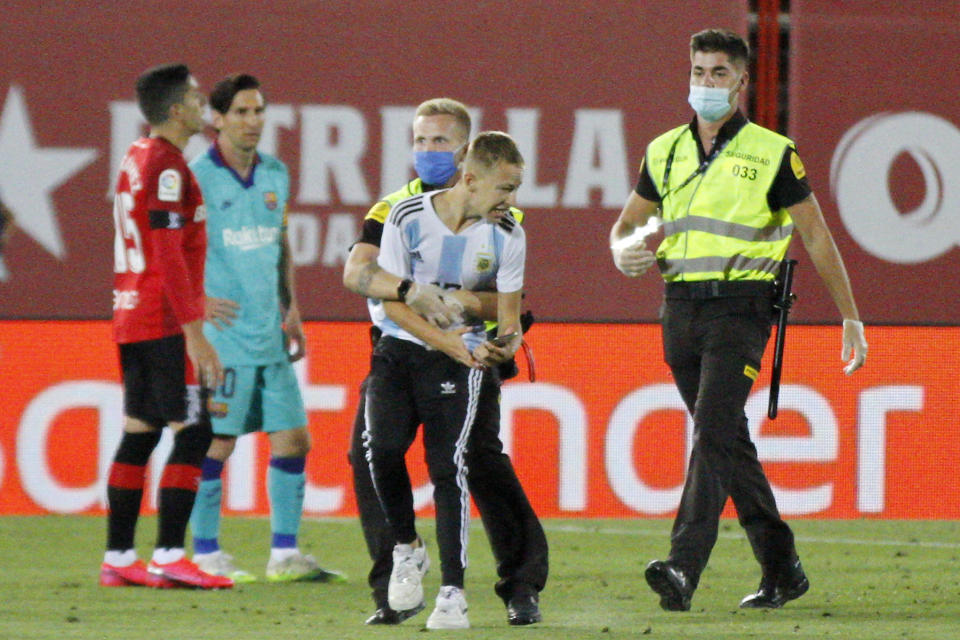 Un hombre con la camiseta de la selección de Argentina es sometido por personal de seguridad tras invadir la cancha del Mallorca, durante un encuentro entre el equipo local y el Barcelona, el sábado 13 de junio de 2020 (AP Foto/Francisco Ubilla)