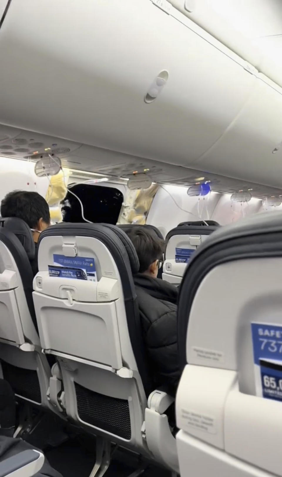 This image from video provided by Elizabeth Le shows passengers near the damage on an Alaska Airlines Boeing 737 Max 9, Flight 1282, which was forced to return to Portland International Airport on Friday, Jan. 5, 2024. (Elizabeth Le via AP)