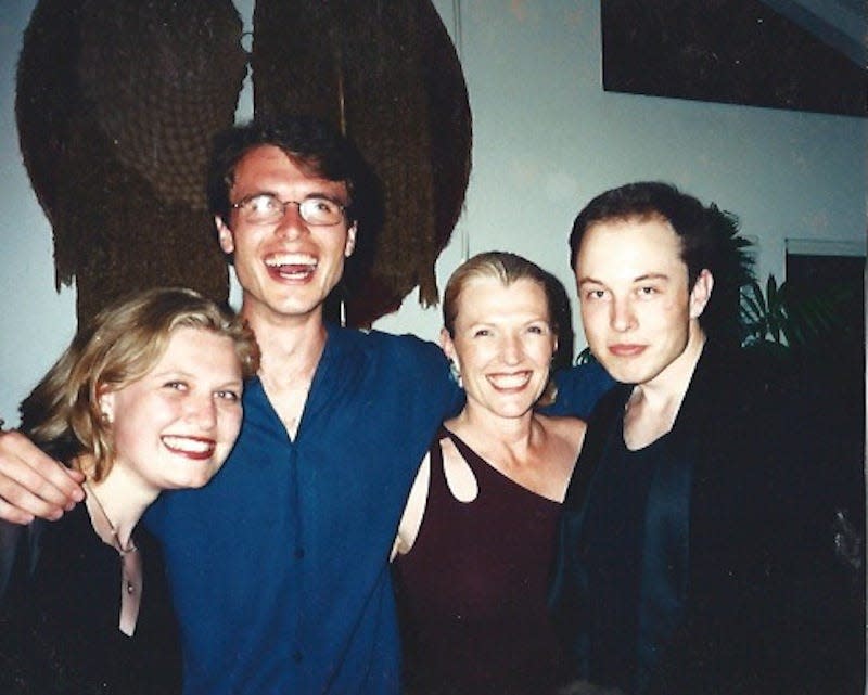 The Musk family posing together at a family gathering in a white room with a potted plant and a large painting.