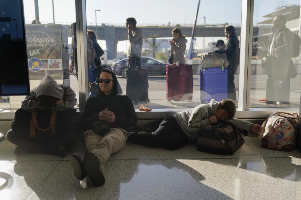 Rome DeGuzman sits on the floor of a terminal next to his two sons on Dec. 19, 2022 after missing a morning flight to Hawaii as travelers wait in line outside the building to check in at the Los Angeles International Airport in Los Angeles. (AP Photo/Jae C. Hong)