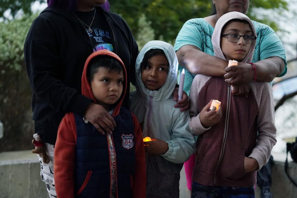 Eric Martinez, 6, left, Isabella Southerland, 7, center, and Andrew Martinez, 9, right, stand with their family as they take part in a community vigil Tuesday night for the dozens of people found dead Monday in a semi-trailer in San Antonio.