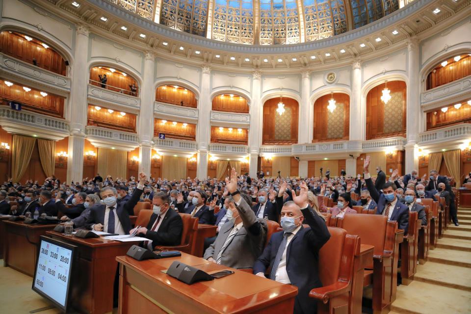 Members of parliament raise their hands while voting on procedural issues before a session called to vote on the government team of Romanian prime minister-designate Florin Citu in Bucharest, Romania, Wednesday, Dec. 23, 2020. Romania's president Klaus Iohannis appointed on Tuesday, the outgoing finance minister as prime minister-designate after three pro-Western center-right groups joined forces to keep out of power a left-leaning populist party that won most votes at a parliamentary election earlier this month. (AP Photo/Vadim Ghirda)