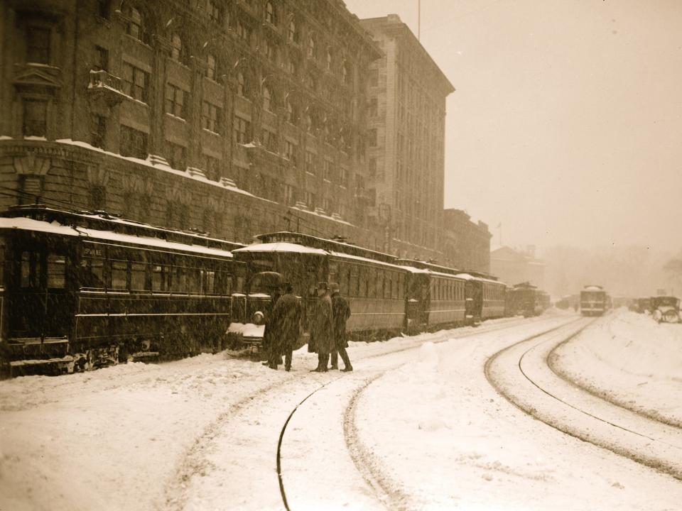 A group of men approach a trolley stuck on the rail line, while other cars are lined up on the city streets during the Knickerbocker blizzard, Washington, DC, 1922.