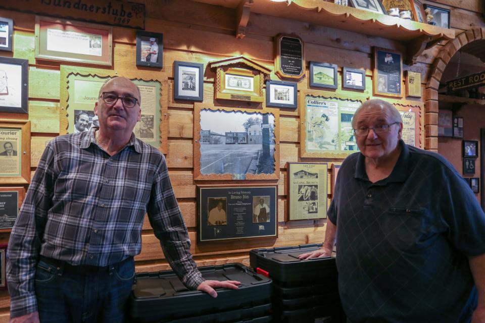 Orlando and Bruno Jr. Itin stand in front of a framed photo of the old Bruno's Pizza location and a plaque of their father as the family remove sports memorabilia off the walls of Bruno's Pizza after officially closing its doors, on Thursday, Feb. 9, 2024, in West Lafayette Ind.