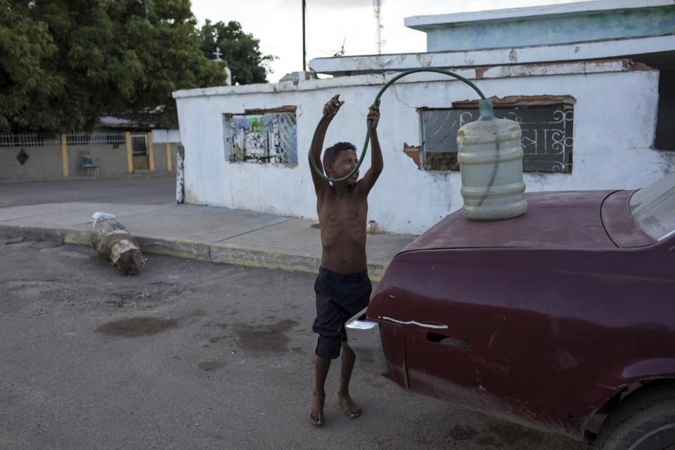 In this Nov. 14, 2019 photo, a boy returns a hose into a jug after siphoning gas into the family car in the "Altos de Milagros Norte" neighborhood in Maracaibo, Venezuela. The downfall of Maracaibo and the lake by the same name has been especially brutal. It was once the hub of Venezuela’s thriving oil industry. Critics blame two decades of socialist rule for destroying the oil industry, that today produces a fraction of what it did at its height two decades ago. The Venezuelan government blames U.S. sanctions for many of its problems. (AP Photo/Rodrigo Abd)