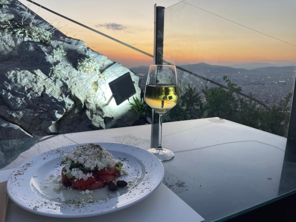 plate of food and glass of wine at a table overlooking mount lycabettus