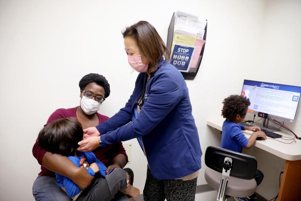 A doctor looks at a child in his mother's lap.