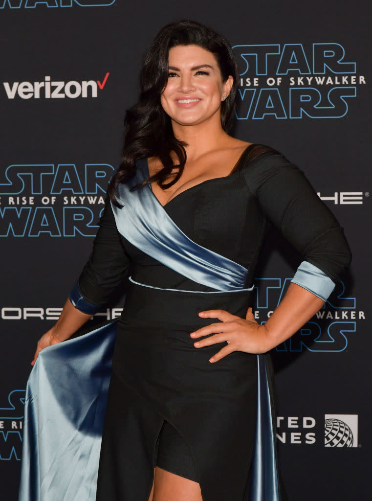 Gina Carano at the "Star Wars: The Rise of Skywalker" premiere, wearing a black dress with a satin blue sash and asymmetrical design