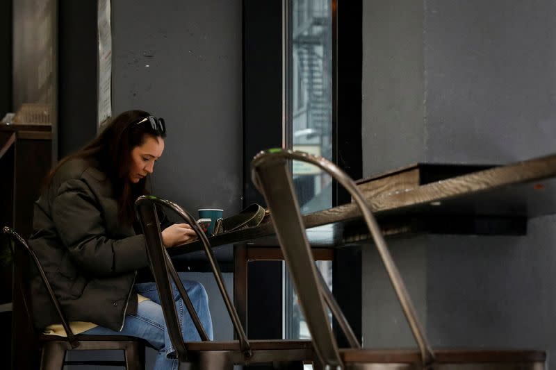 FILE PHOTO: A patron uses her phone and drinks a coffee inside a coffee shop, on the first day of the return to indoor dining for New York