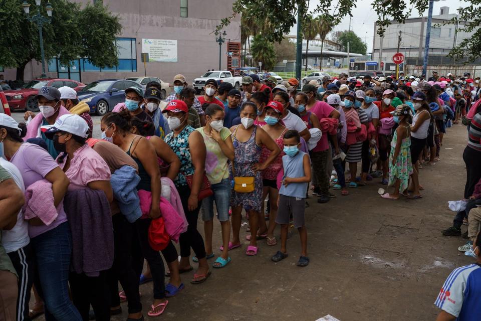 Hundreds of people are standing in a crowded line on a dirt road.