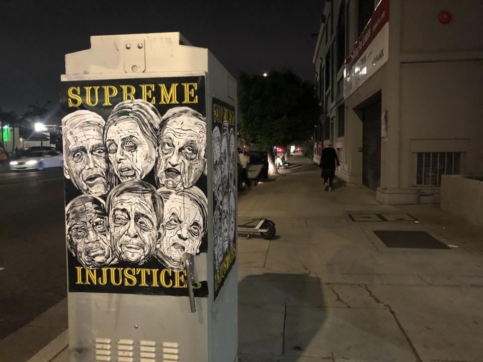 A poster that shows six members of the Supreme Court that overturned Roe v. Wade, pasted to an electrical box at night.