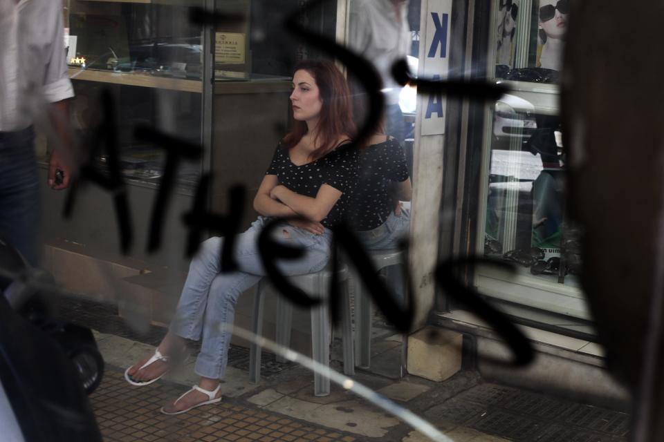 A woman is reflected in a graffiti-covered mirror as she waits for customers outside her sign-making shop in central Athens on Thursday, Aug. 30, 2012. Greek Prime Minister Antonis Samaras promised his austerity-weary countrymen on Thursday that new spending cuts planned for 2013-14 will be the last, but warned that without them the nation would have to leave the 17-member eurozone. (AP Photo/Petros Giannakouris)