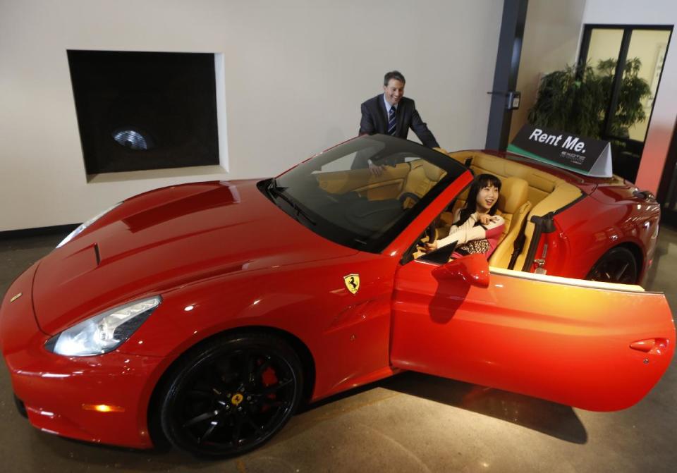 In this Wednesday, March, 26, 2014 photo, Adam Belsky, Enterprise Exotic Car Collection manager shows Jingyi Yang, 21, from Seattle a 2014 Ferrari California displayed for rent at the Enterprise Exotic Car Collection showroom near Los Angeles International Airport. (AP Photo/Damian Dovarganes)