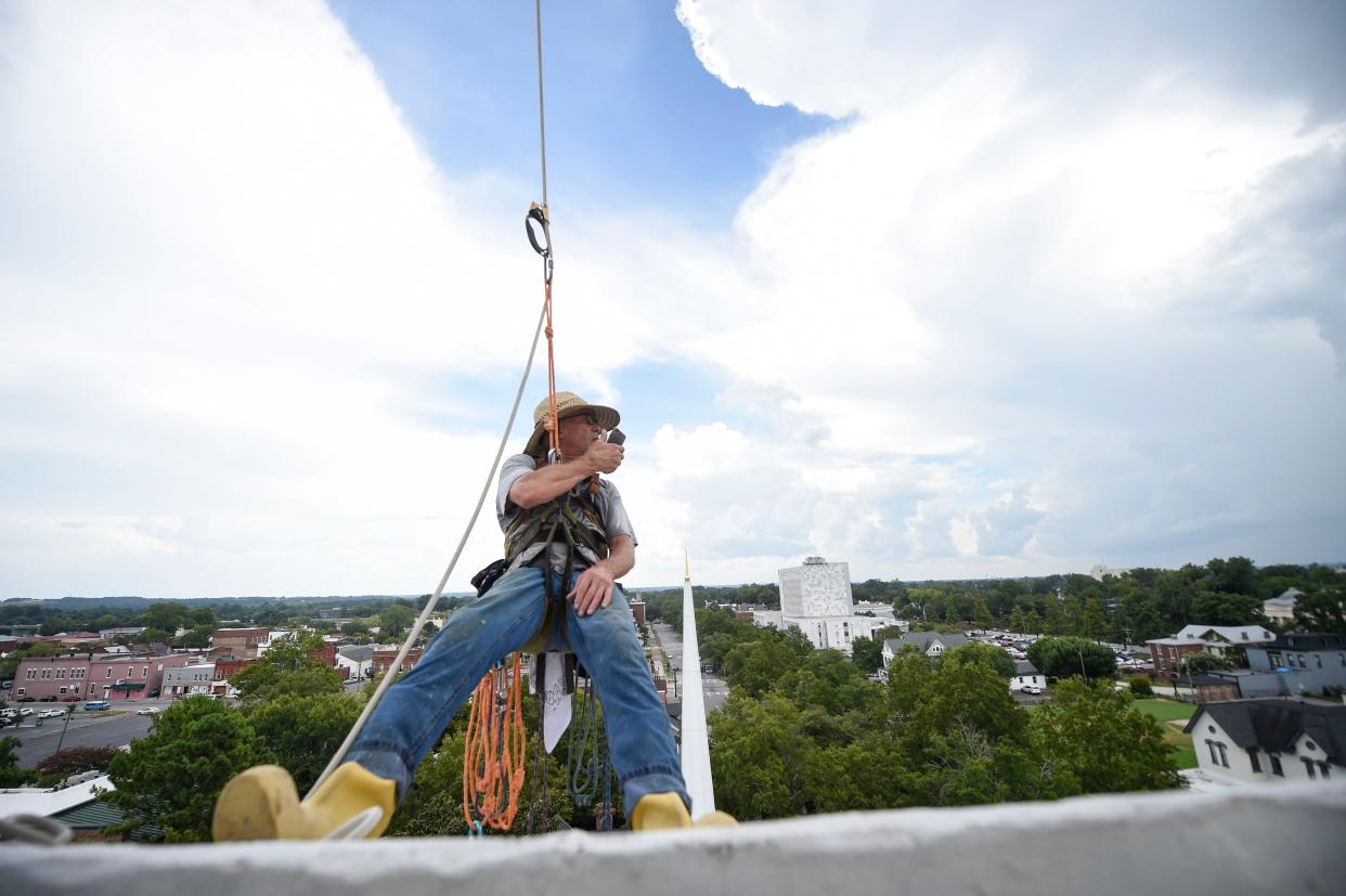 Steeplejack Fred Franklin calls a friend on the ground about the upcoming storm at First Christian Church on Wednesday, Aug. 3, 2022. Franklin was unable to paint due to thunderstorms coming from the north.