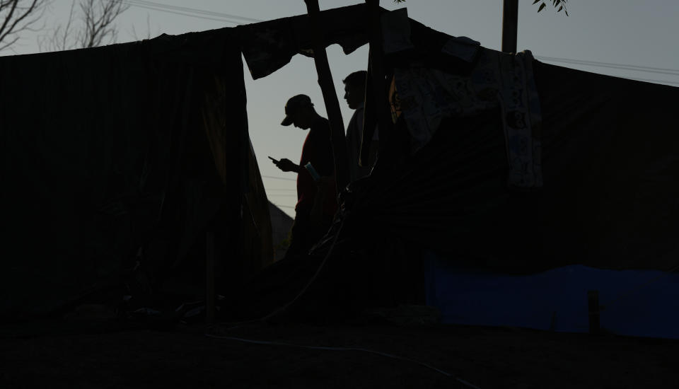 A Venezuelan migrant texts at a makeshift camp set up alongside a river bank in Matamoros, Mexico, Thursday, Dec. 22, 2022. Migrants are waiting on a pending U.S. Supreme Court decision on asylum restrictions. (AP Photo/Fernando Llano)