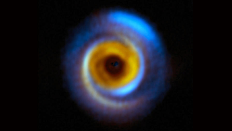 A composit image of a planet-forming disk in deep space with blue and yellow hues of different wavelengths.