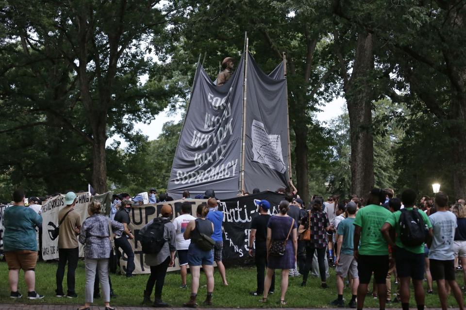 FILE - In this Monday, Aug. 20, 2018 file photo, banners are used to cover the statue known as Silent Sam as people gather during a rally to remove the confederate statue from campus at the University of North Carolina in Chapel Hill, N.C. Police are filing charges against three people who they say helped bring down the Confederate statue at North Carolina's flagship university. University of North Carolina Police issued a statement Friday, Aug. 24, 2018, that the department has filed warrants for three people on charges of misdemeanor rioting and defacing a public monument. (AP Photo/Gerry Broome, File)