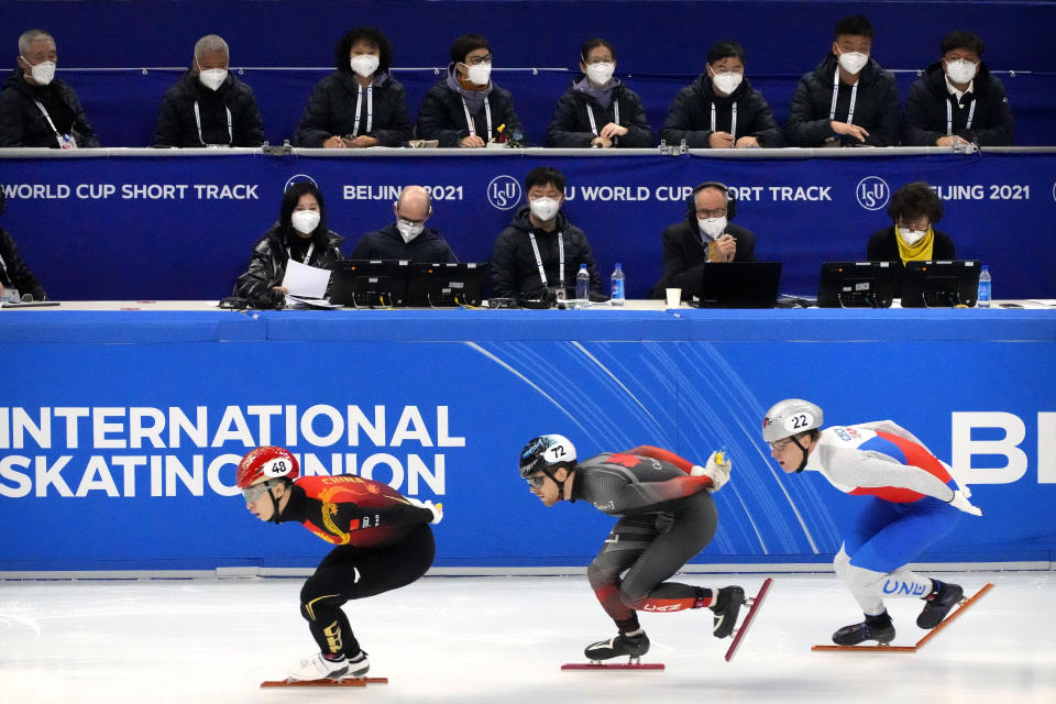 Race officials wearing face masks to protect against COVID-19 watch as skaters compete in a preliminary for men's 1000m at the ISU World Cup Short Track speed skating competition, a test event for the 2022 Winter Olympics, at the Capital Indoor Stadium in Beijing, Friday, Oct. 22, 2021. (AP Photo/Mark Schiefelbein)