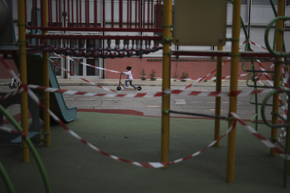 A girl rides a scooter by a prohibited playground in the schoolyard of the Saint-Tronc Castelroc primary school in Marseille, southern France, Thursday, May 14, 2020. The school can only operate three classroom since the others could not be disinfected. The government has allowed parents to keep children at home amid fears prompted by the COVID-19. (AP Photo/Daniel Cole)