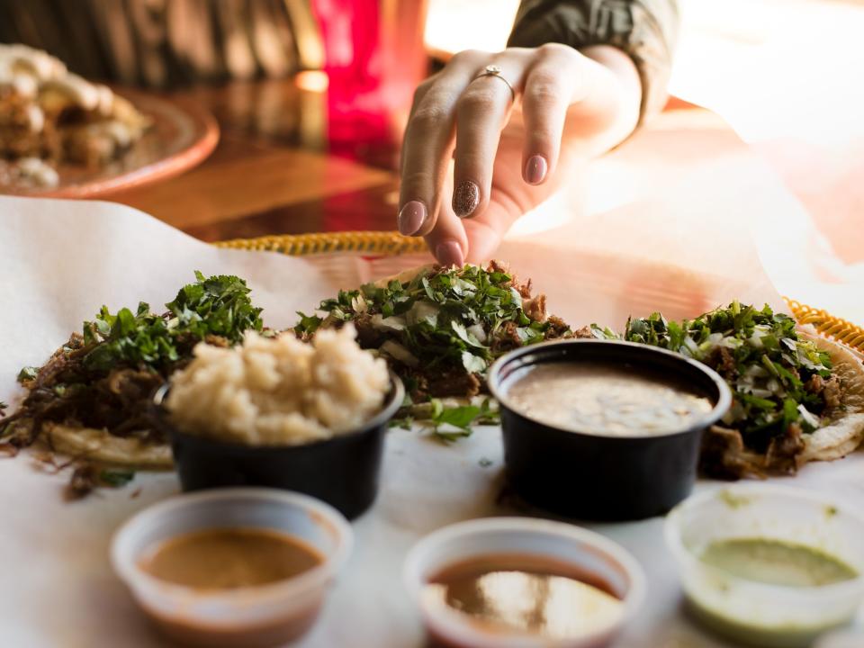 a plate of three tacos with a hand grabbing for one