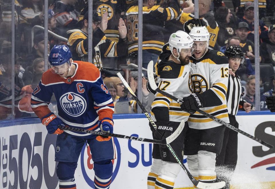 Boston Bruins' Nick Foligno (17) and Charlie Coyle (13) celebrate after a goal as Edmonton Oilers' Connor McDavid (97) skates past during first-period NHL hockey game action in Edmonton, Alberta, Monday, Feb. 27, 2023. (Jason Franson/The Canadian Press via AP)