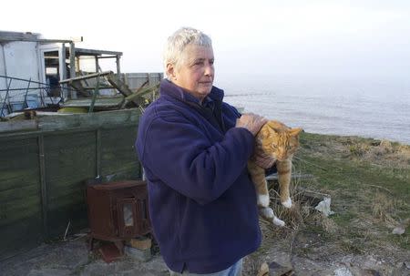 Bryony Nierop-Reading, a 69-year-old pensioner, holds her cat as she stands by the remains of her bungalow that was demolished by the local Happisburgh council after a winter storm eroded the coastline and left it perched over the edge of a cliff, March 12, 2014. REUTERS/Alister Doyle