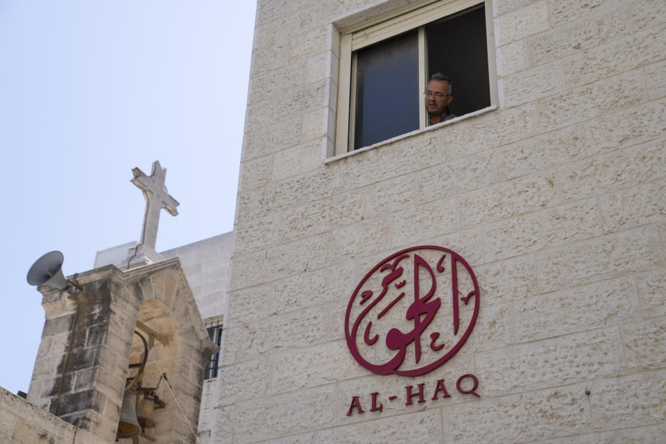 A man looks out of the window of the office of al-Haq Human rights organization that is adjacent to the St. Andrew's Anglican Episcopal Church, in the West Bank city of Ramallah, Thursday, Aug. 18, 2022. Israel raided the offices of several Palestinian advocacy groups, including al-Haq, sealing entrance doors and leaving notices declaring them closed, the groups said Thursday. (AP Photo/Nasser Nasser)