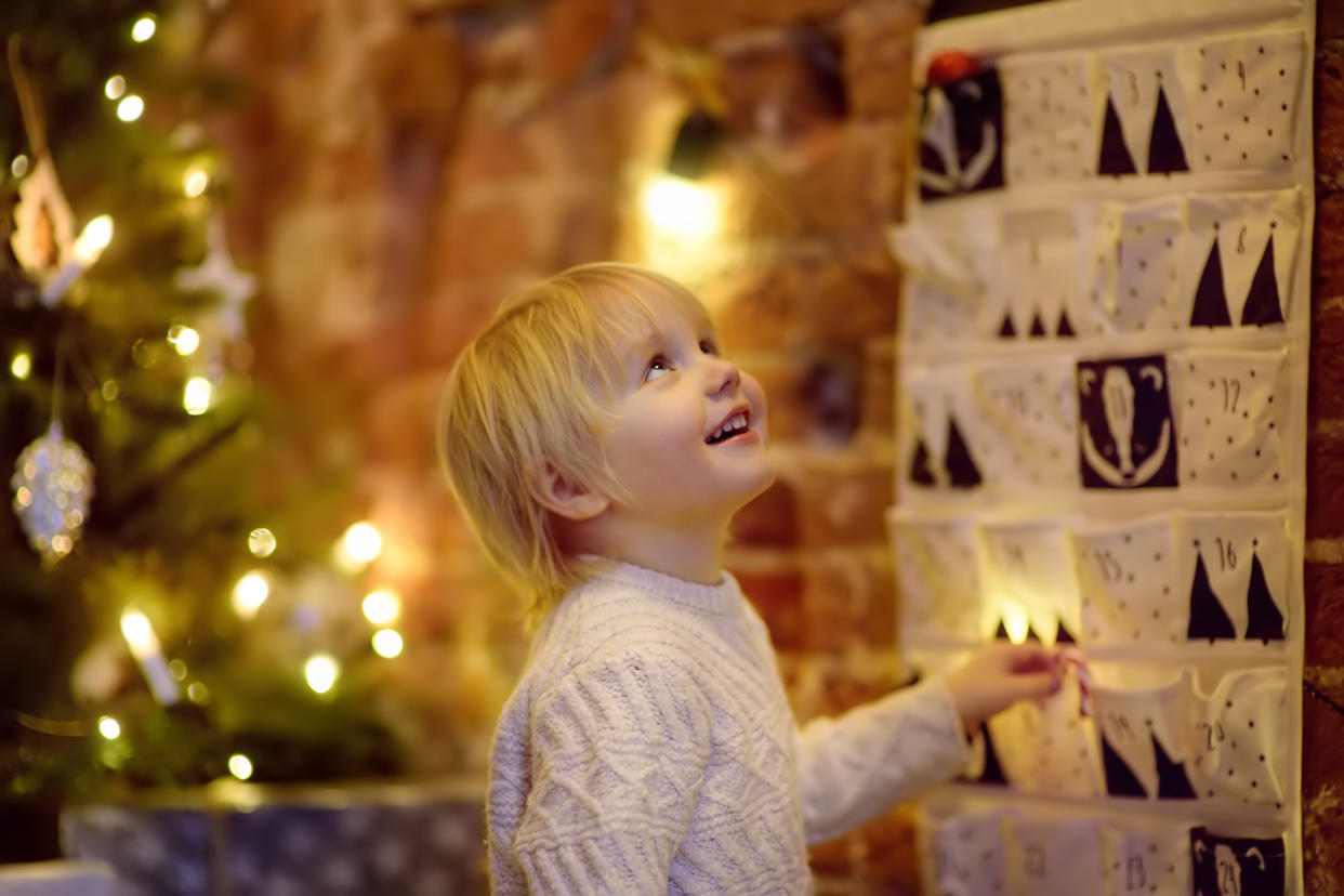 Happy little boy takes sweet from advent calendar on Christmas eve. Traditional christmas calendar for kids