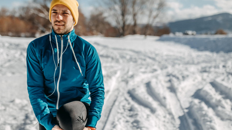 A man stops to stretch while running in the snow