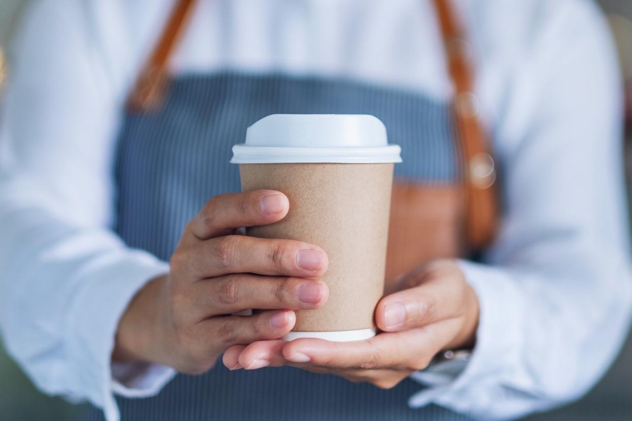 A waitress holding and serving a paper cup of hot coffee