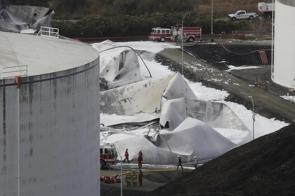 Fire and emergency crews walk past damage at NuStar Energy fuel storage facility, Wednesday, Oct. 16, 2019, in Crockett, Calif. Officials are trying to determine if a 4.5 magnitude earthquake the day before triggered an explosion at the facility. (AP Photo/Jeff Chiu)