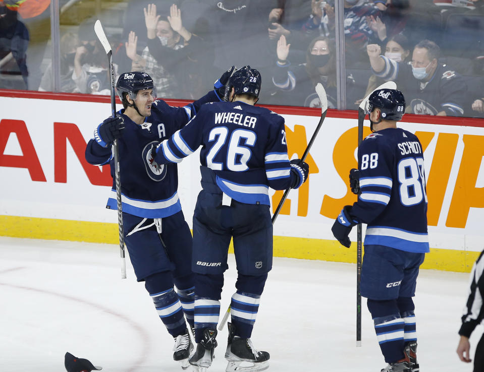 Winnipeg Jets' Mark Scheifele (55), Blake Wheeler (26), and Nate Schmidt (88) celebrate Scheifele's hat-trick goal against the New Jersey Devils, during the third period of an NHL hockey game Friday, Dec. 3, 2021, in Winnipeg, Manitoba. (John Woods/The Canadian Press via AP)