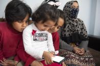 Bayan, left, Safa, center, and Iman play with a cellphone as they sit next to their mother Kariman, 32 at their apartment in the northern city of Thessaloniki, Greece, Saturday, May 1, 2021. Sundered in the deadly chaos of an air raid, a Syrian family of seven has been reunited, against the odds, three years later at a refugee shelter in Greece's second city of Thessaloniki. (AP Photo/Giannis Papanikos)