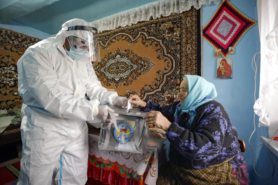 An election official wearing a biohazard suit, for protection against the COVID-19 infection, holds a mobile ballot box as an elderly lady casts her vote in the presidential elections in Hrusova, Moldova, Sunday, Nov. 15, 2020. Moldovans returned to the polls Sunday for the second round of voting in the country's presidential election, facing a choice between the staunchly pro-Russian incumbent and his popular pro-Western challenger after former prime minister, Maia Sandu, who beat the odds to win the first round on November 1 with over 36 percent of to vote, leaving the incumbent, President Igor Dodon, trailing her by over 3.5 points. (AP Photo/Roveliu Buga)