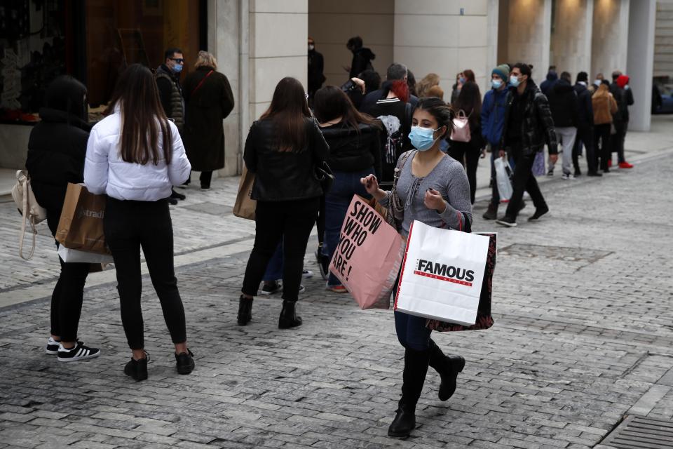 Youths stand in a queue as they wait to enter a clothes shop on Ermou Street, Athens' main shopping area, Friday, Jan. 22, 2021. Greece's government has extended nationwide lockdown measures indefinitely but retail stores and malls reopened Monday with strict entrance limits. (AP Photo/Thanassis Stavrakis)