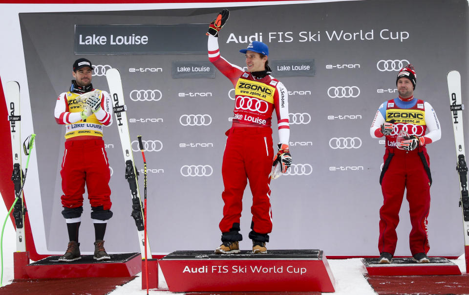 First place finisher Matthias Mayer, of Austria, celebrates on the podium with second place finisher Austria's Vincent Kriechmayr, left, and third place finisher Switzerland's Beat Feuz after the men's World Cup downhill ski race in Lake Louise, Alberta, Saturday, Nov. 27, 2021. (Jeff McIntosh/The Canadian Press via AP)