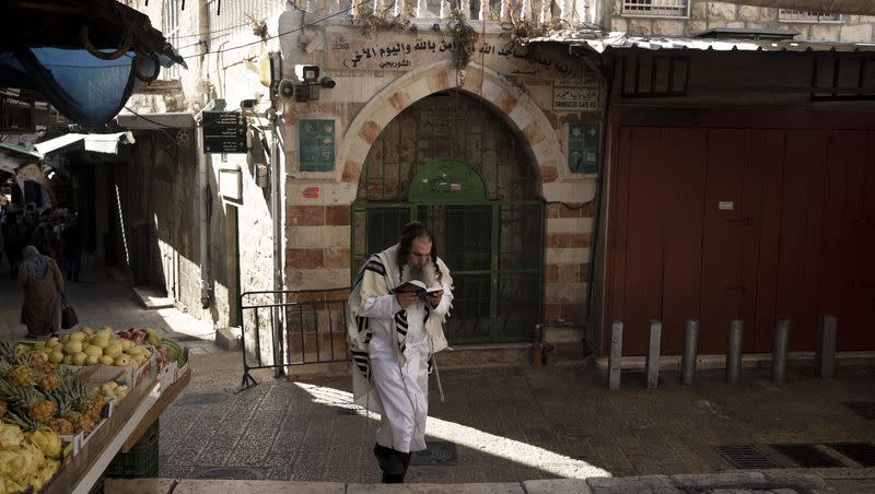 A Jewish worshipper reads from a prayer book on Yom Kippur, the Jewish Day of Atonement, as he walks in the Old City of Jerusalem, Monday, Sept. 25, 2023.