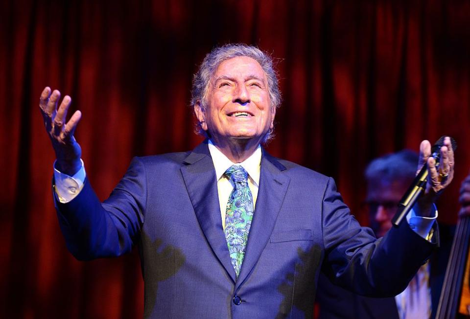 singer tony bennett pictured with a microphone in his hand while performing on stage, smiling looking up
