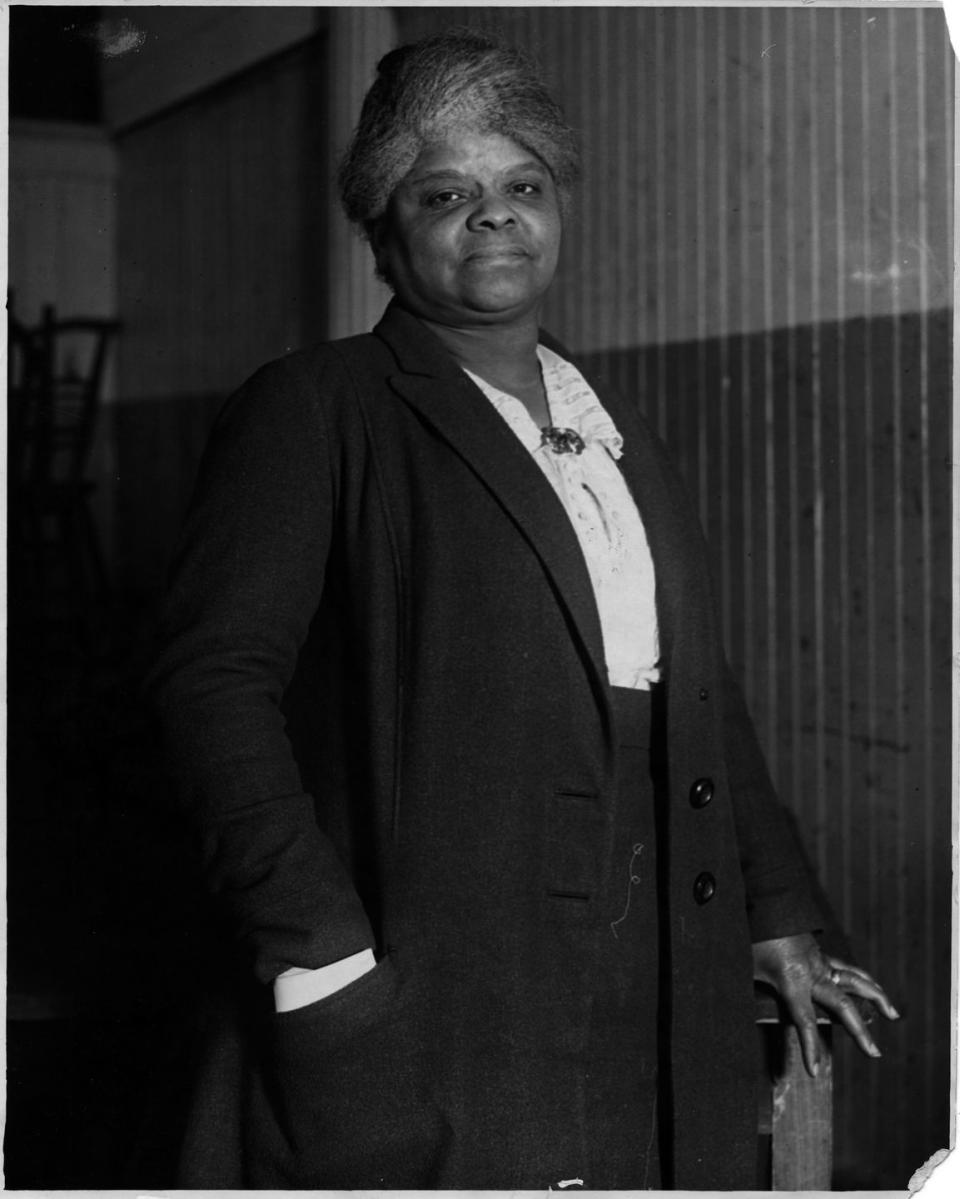 ida b wells stands and looks at the camera, she wears a long jacket, light colored blouse and dark bottoms