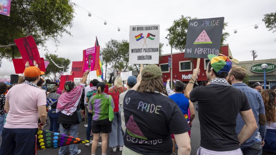 People are seen from behind on a parade route carrying handmade signs.