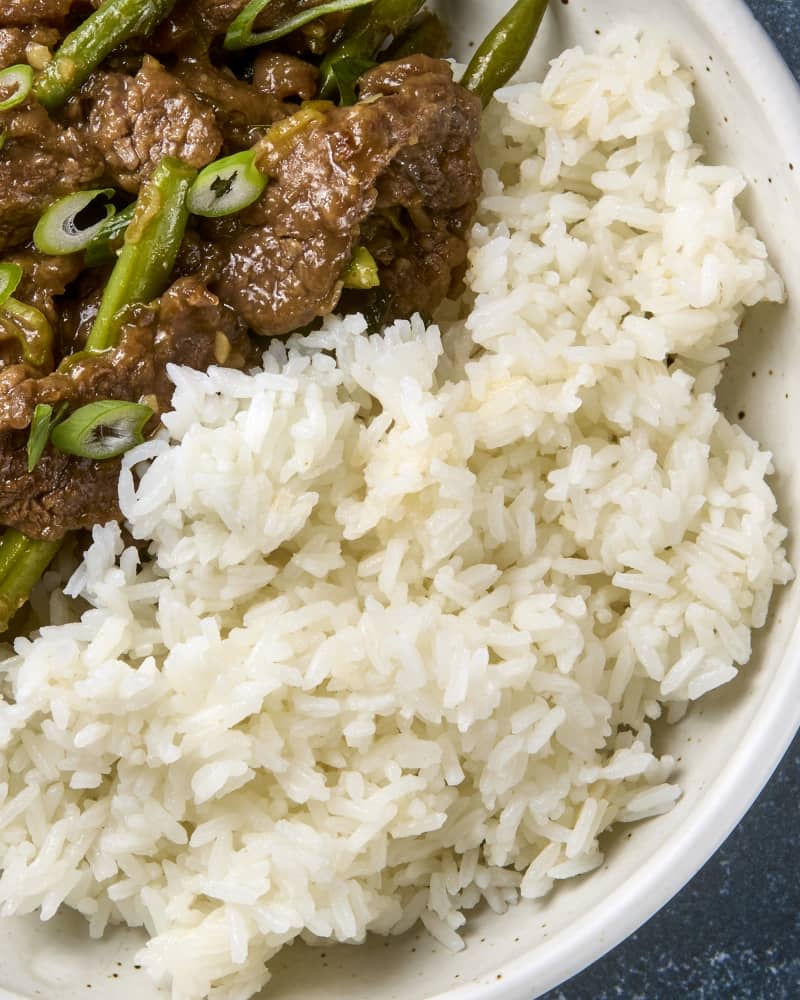 Cooked jasmine rice on the side of a beef dish.