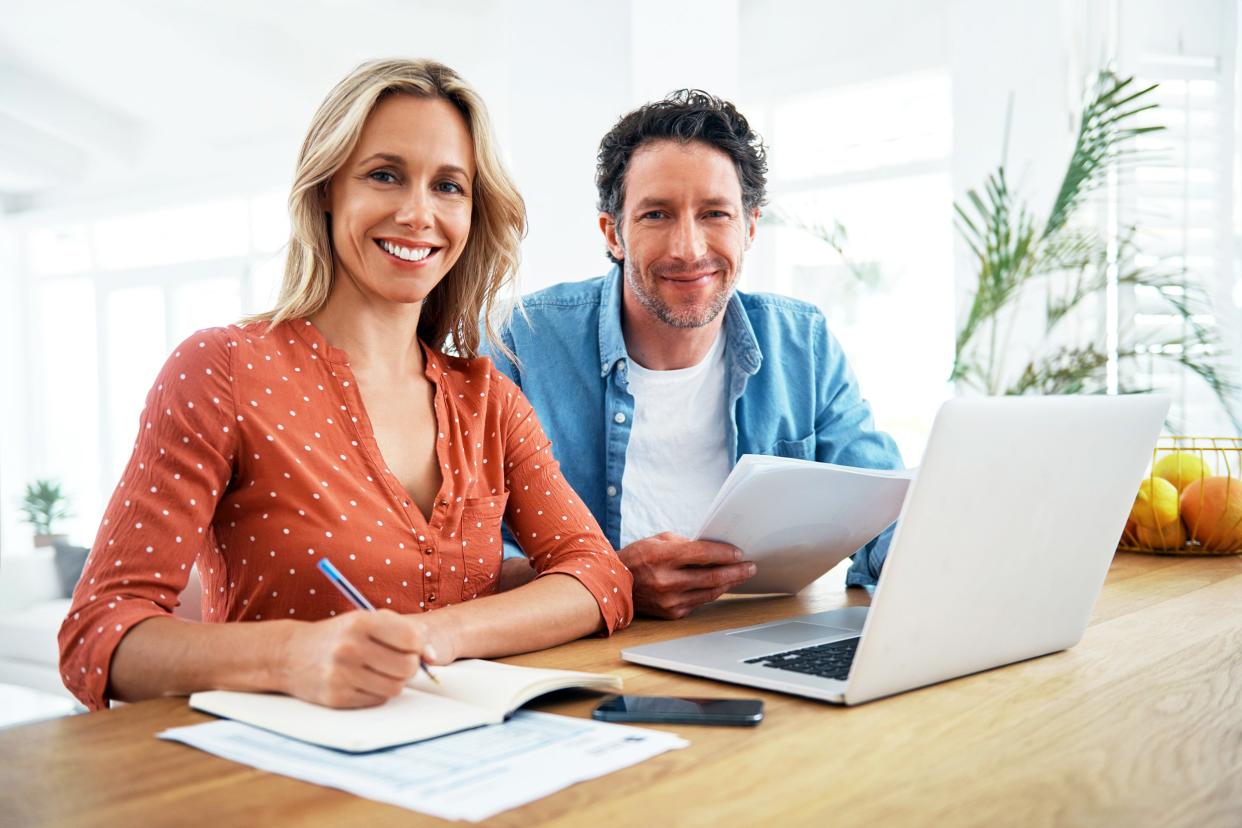 Couple paying bills at home and smiling at camera