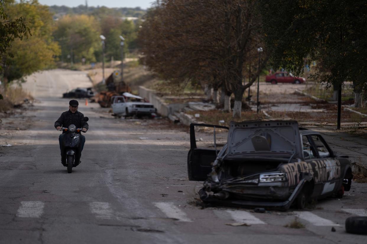 A man drives his motorcycle past destroyed cars in the retaken village of Velyka Oleksandrivka, Ukraine, Wednesday, Oct. 12, 2022.