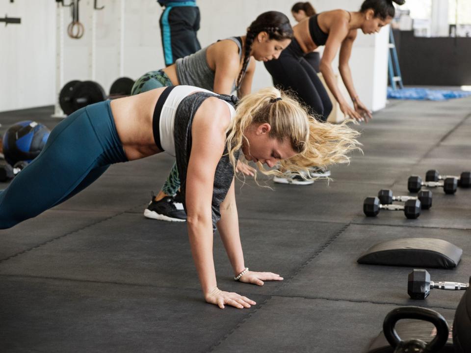 three athletes in various stages of burpee exercises in a gym