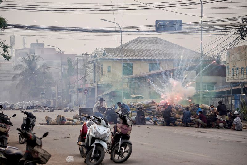 Firecrackers explode as protestors take cover behind a barricade during a demonstration against the military coup in Mandalay